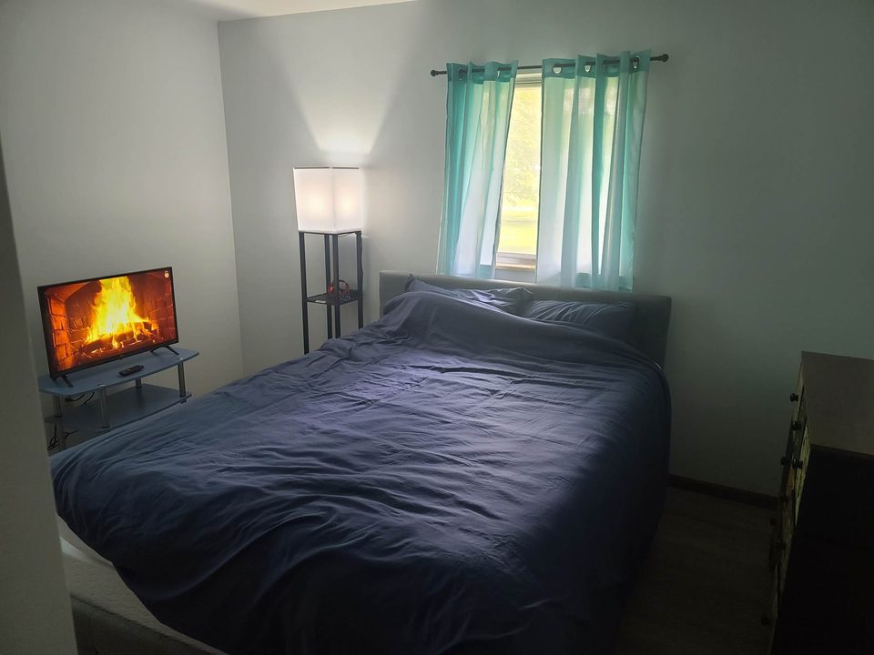 Main bedroom with a queen bed, TV, and teal curtains